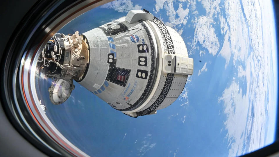  A white space capsule is seen through a spacecraft window, with earth in the background. 