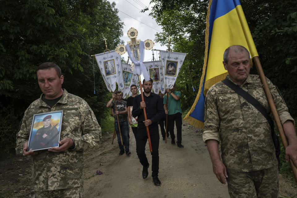 Ukrainian servicemen carry a National flag and a photograph of Ukrainian serviceman Bohdan Kobylianskyi who was killed in Donbas, during the funeral ceremony in Dusaniv, Ukraine, Saturday, July 22, 2023. (AP Photo/Evgeniy Maloletka)