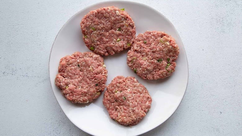 uncooked burger patties on white plate