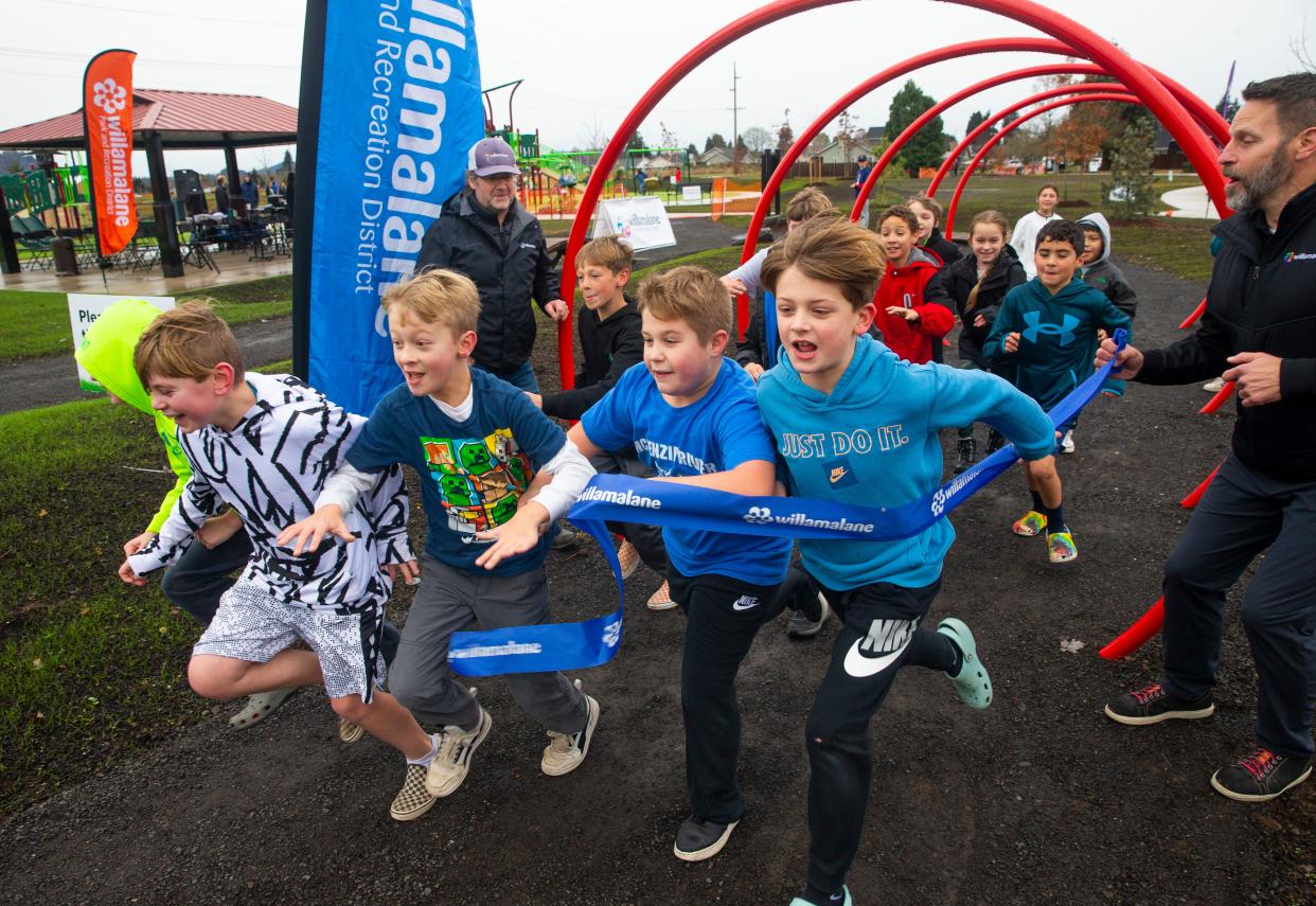 Children from a nearby school run through a ribbon held by Willamalane Park and Recreation District Landscape Architect Simon Daws, background left, and Executive Director Michael Wargo during a dedication of the new Arrow Park in Springfield in December 2022.