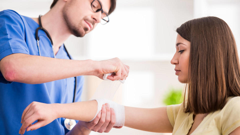 Confident male doctor is bandaging upper limb of young woman.