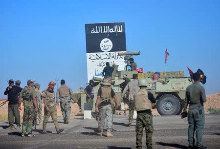 Shi'ite Popular Mobilization Forces (PMF) and Iraqi army members gather next to the black flag sign commonly used by Islamic State militants, on the outskirts of Hawija, Iraq, October 4, 2017. REUTERS/Stringer