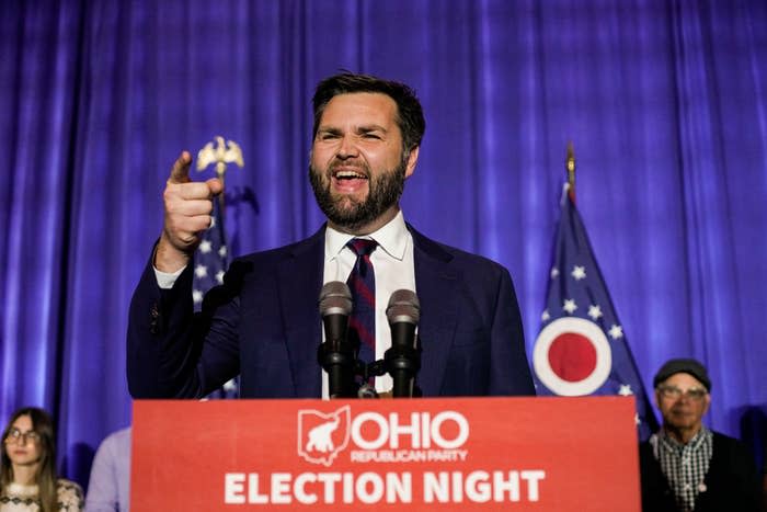 J.D. Vance speaks passionately at the podium of Ohio Republican Party election night event, with people standing behind him and Ohio state flags visible in the background