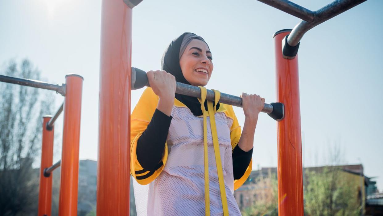 calisthenics at outdoor gym, young woman doing pull up on exercise equipment