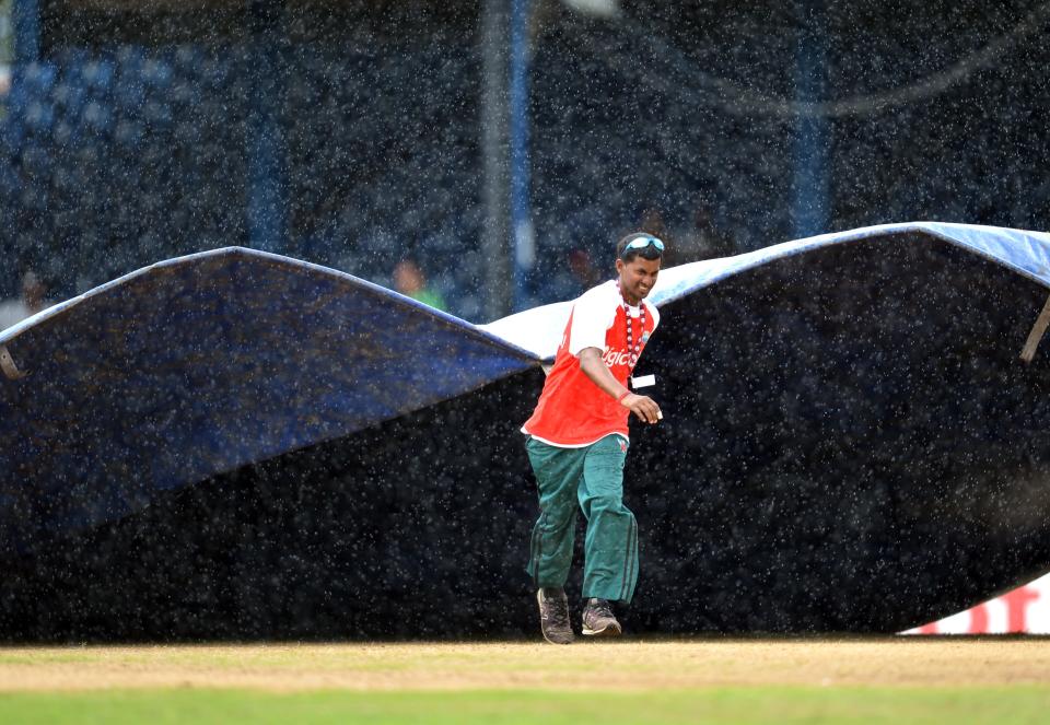 A member of the grounds crew pulls out a tarp to cover the pitch as rain falls during the second day of the second-of-three Test matches between Australia and West Indies April 16, 2012 at Queen's Park Oval in Port of Spain. AFP PHOTO/Stan HONDA (Photo credit should read STAN HONDA/AFP/Getty Images)