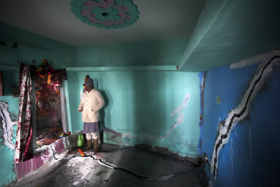 Chandra Pandey, 66, stands in front of the worship area inside his house with big, deep cracks on the walls in Joshimath, India's Himalayan mountain state of Uttarakhand, Jan. 20, 2023. Big, deep cracks had emerged in over 860 homes in Joshimath, where they snaked through floors, ceilings and walls, making them unlivable. Roads were split with crevices and multi-storied hotels slumped to one side. Authorities declared it a disaster zone and came in on bulldozers, razing down whole parts of a town that had become lopsided. (AP Photo/Rajesh Kumar Singh)