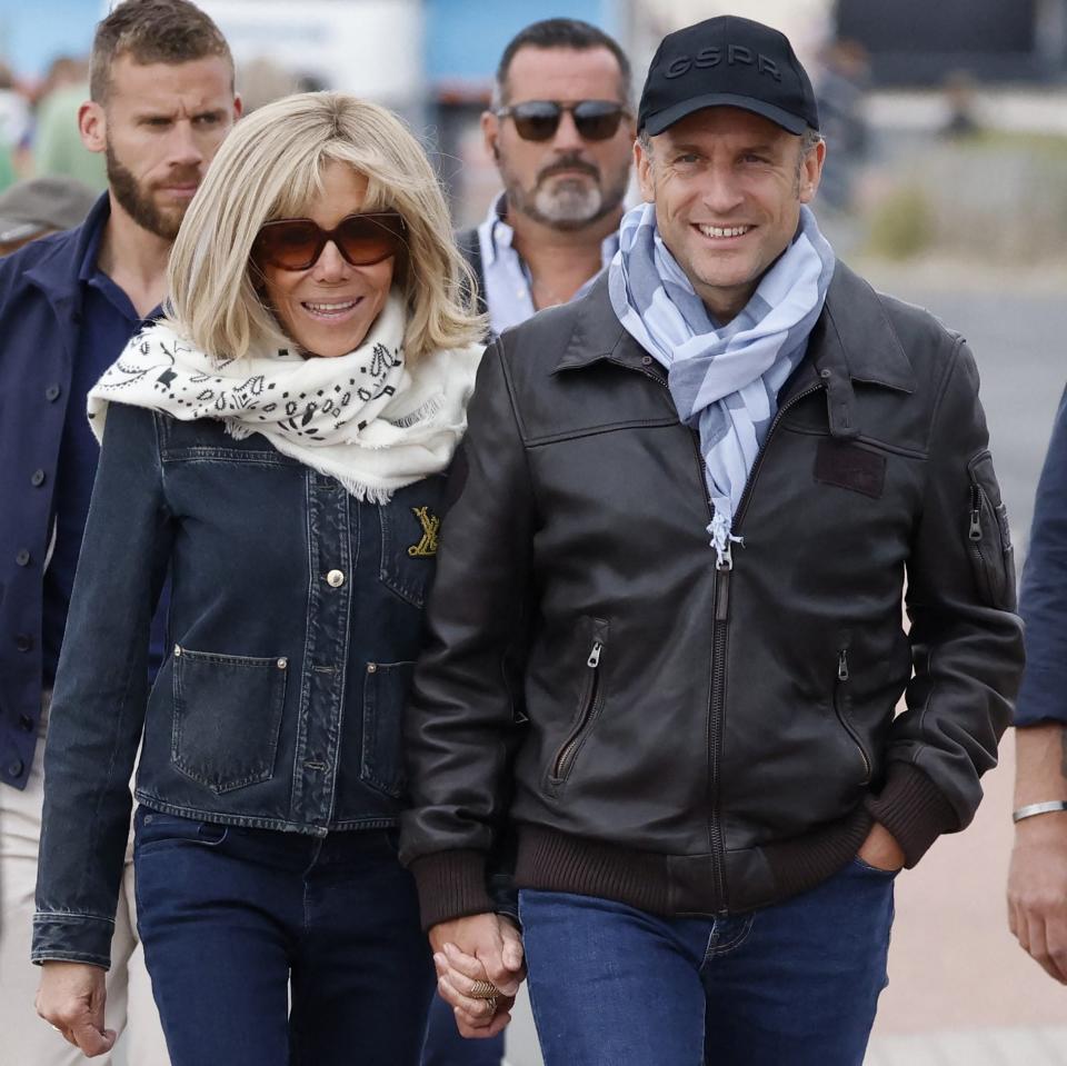 Mr Macron wears a baseball cap, scarf and leather jacket as he walks with his wife - his sunglasses are not visible