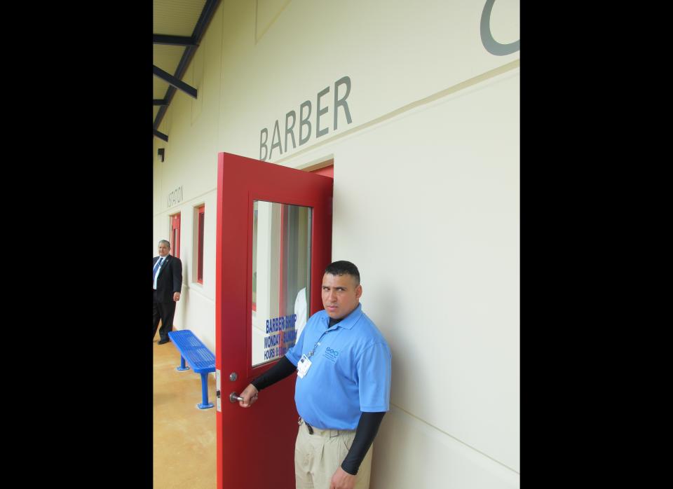 A guard holds open a door to the barber shop at a new civil detention facility for low-risk inmates in Karnes City, Texas, on Tuesday, March 13, 2012. Federal officials are holding up the new facility as the centerpiece of an initiative to treat those facing immigration violation charges more humanely after lawsuits filed in past years. (AP Photo/Will Weissert)