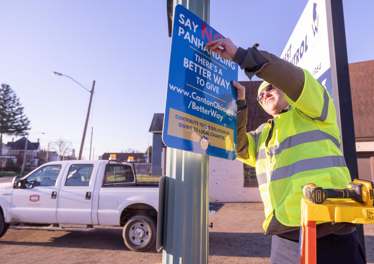 Matthew Bissett, a laborer with Canton Engineering's traffic, signs and paint department, fastens a sign onto a light post at the corner of 12th Street and McKinley Avenue on Thursday. The sign encourages passersby to give their money to local charities that help people living in poverty rather than giving their money to panhandlers.