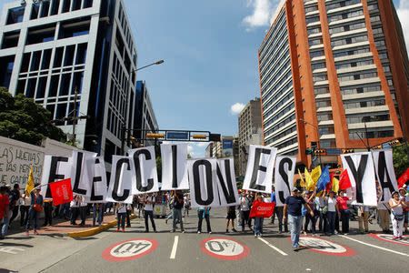 Opposition supporters hold placards that read "Elections now" during a rally against Venezuelan President Nicolas Maduro's government and to commemorate the 59th anniversary of the end of the dictatorship of Marcos Perez Jimenez in Caracas, Venezuela January 23, 2017. REUTERS/Christian Veron