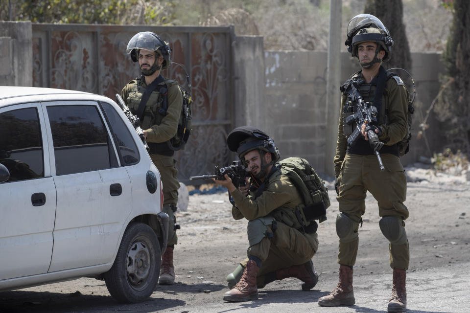 An Israeli soldier aims his weapon at Palestinians protesting against the creation of a new road for Israeli settlers, near the Palestinian village of Beita, north of the West Bank city of Nablus, Wednesday, Aug. 25, 2021. (AP Photo/Majdi Mohammed)