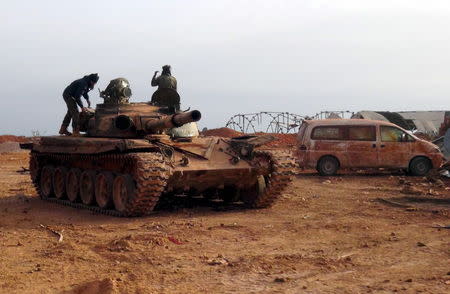 Islamist rebel fighters stand on a tank that belonged to forces loyal to Syria's President Bashar al-Assad in Qarmeed camp after the rebels took control of the area, April 26, 2015. REUTERS/Abdalghne Karoof