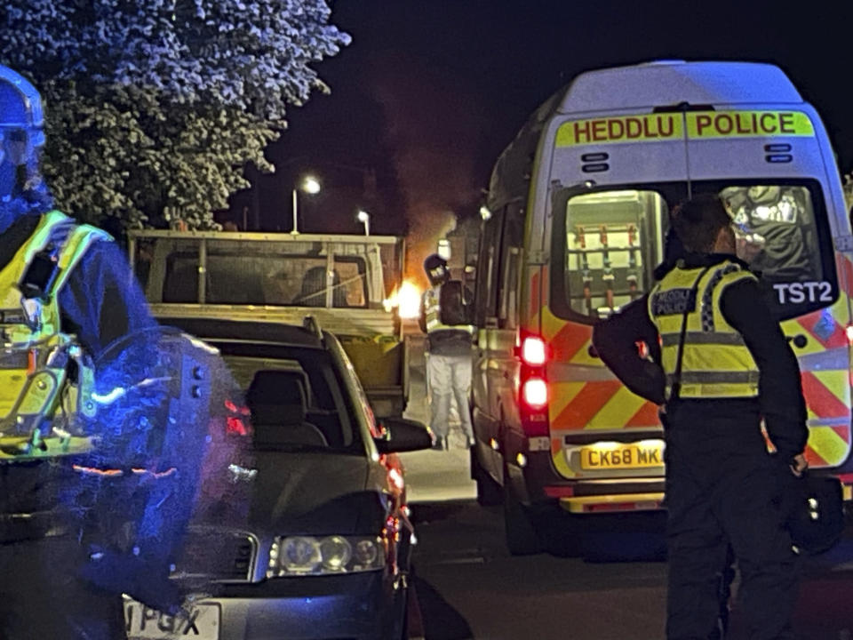 Police officers stand guard on Howell Road in Cardiff as they face a "large scale disorder" at the scene of a serious road traffic collision on Snowden Road in Ely, Cardiff, Tuesday, May 23, 2023. A few cars were set on fire and objects were hurled at police after a traffic accident Monday night in the Welsh capital Cardiff grew into what officials described as “large-scale disorder.”(Bronwen Weatherby/PA via AP)