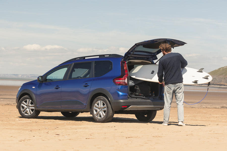 Man loads surfboard into Dacia Jogger boot