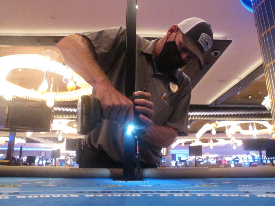 In this June 24, 2020 photo, Dean Loveland, a worker at the Hard Rock casino in Atlantic City N.J., installs plexiglass barriers between player positions at a card table at the casino a week before it was to reopen amid the coronavirus outbreak. Smoking, drinking and eating will all be prohibited when Atlantic City's casinos reopen after being shut for three months due to the coronavirus outbreak under rules imposed by New Jersey Gov. Phil Murphy on June 29, 2020. (AP Photo/Wayne Parry)