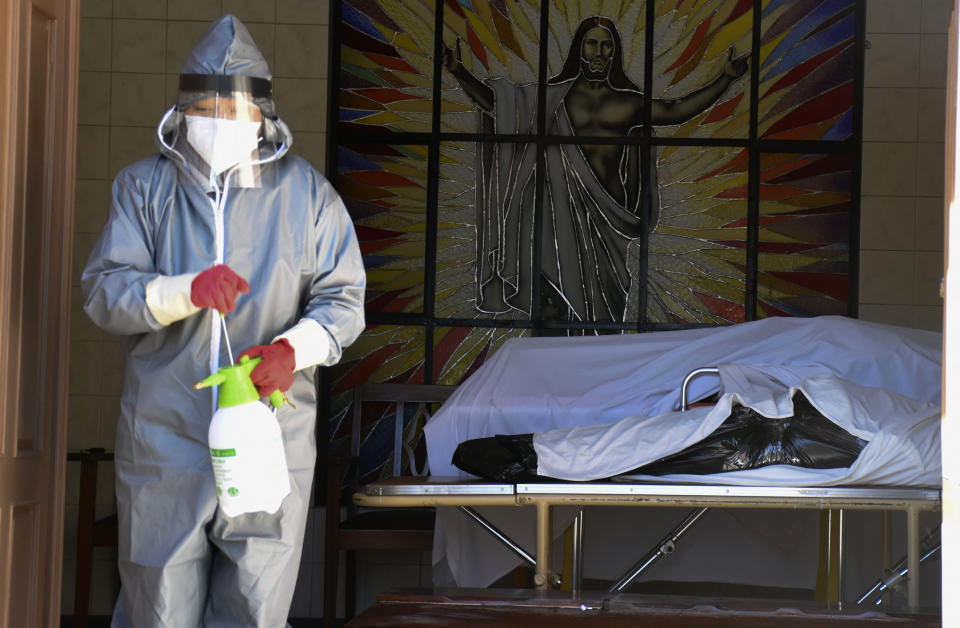 A health worker disinfects the area next to a coffins with the remains of a recently deceased resident of the San Jose nursing home in Cochabamba, Bolivia, Thursday, July 16, 2020. According to city officials, ten elder residents of the care facility have died in the last two weeks after COVID-19 related symptoms. (AP Photo/Dico Solis)