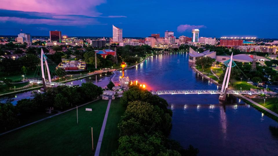 Drone aerial view of downtown Wichita Skyline features Exploration Place on Arkansas River and Keeper of Prairie Indian Sculptor with flames out of water, Kansas.