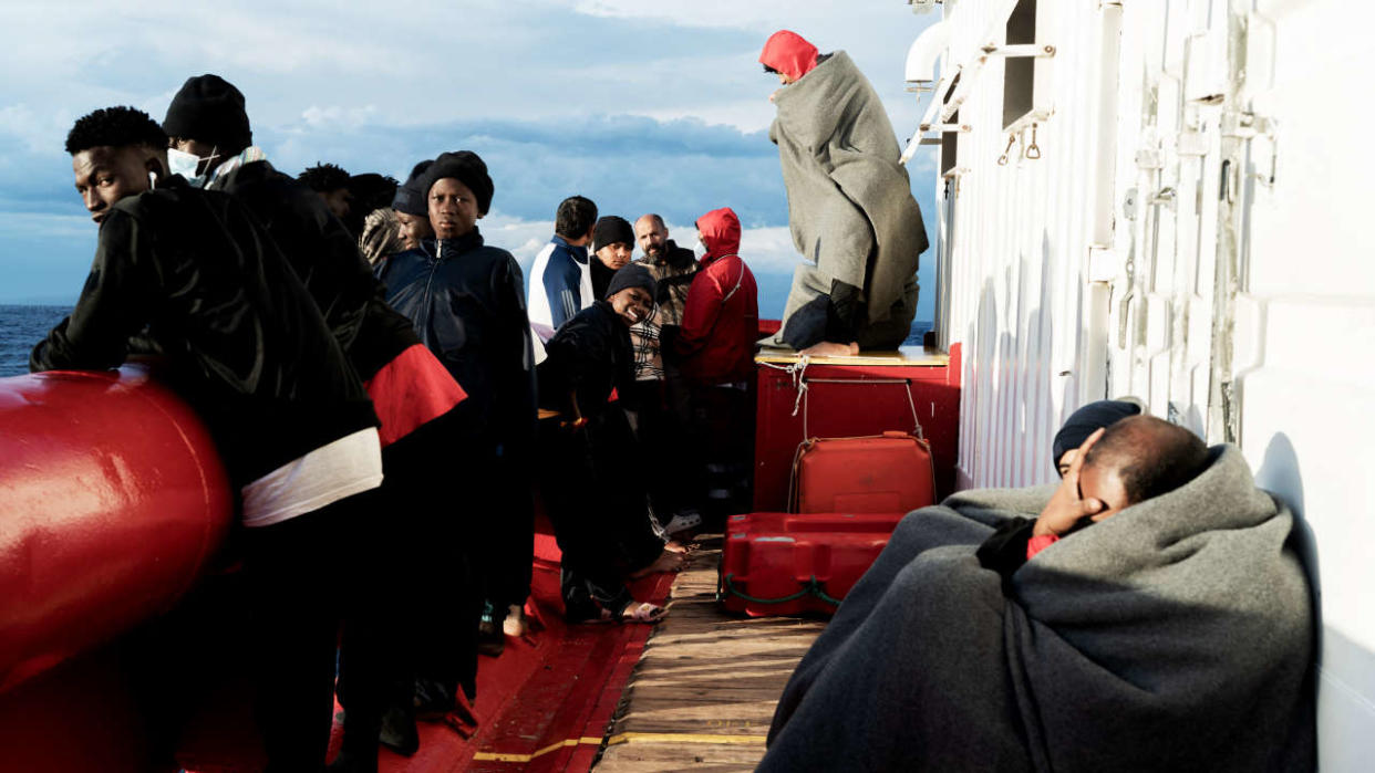 Migrants look on and wait on the deck of the 