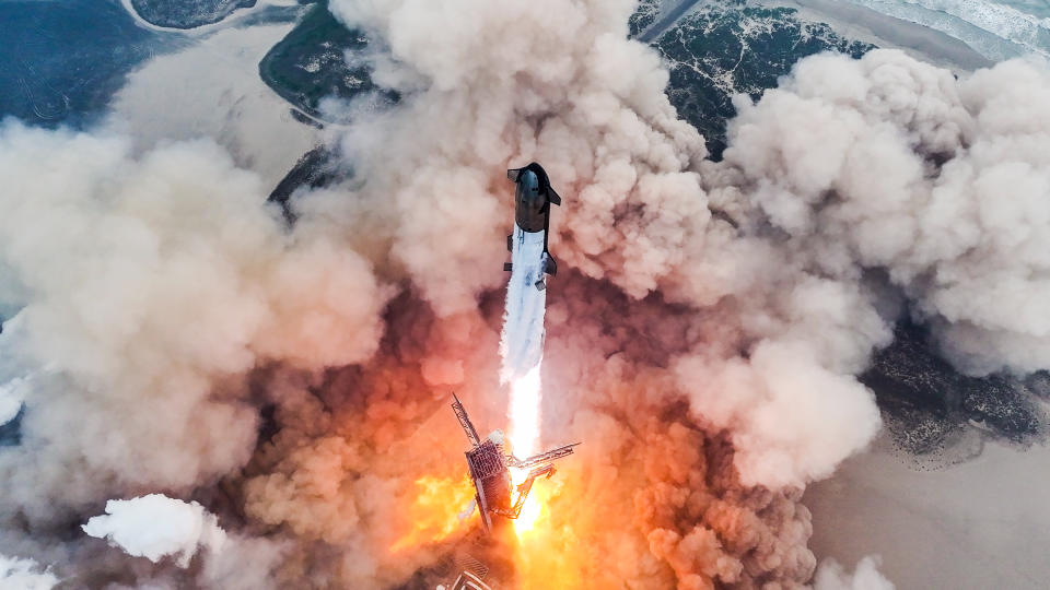     Blick von oben auf eine riesige silberne Rakete, die startet und eine riesige Staubwolke erzeugt. 