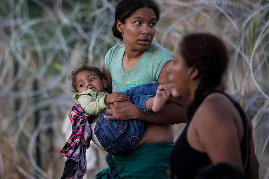 FILE – A woman carries her child after she and other migrants crossed the Rio Grande and entered the U.S. from Mexico, to be processed by U.S. Customs and Border Protection, on Sept. 23, 2023, in Eagle Pass, Texas. President Joe Biden has ordered a halt to asylum processing at the U.S. border with Mexico when arrests for illegal entry top 2,500 a day, which was triggered immediately. (AP Photo/Eric Gay, File)