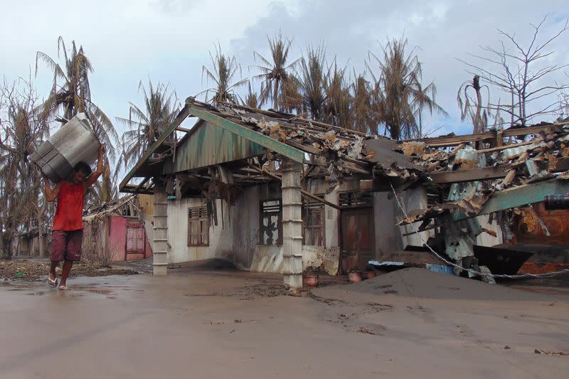 A person carries his belongings as he walks past a damaged house affected by the eruption of Mount Ruang volcano in Laingpatehi village