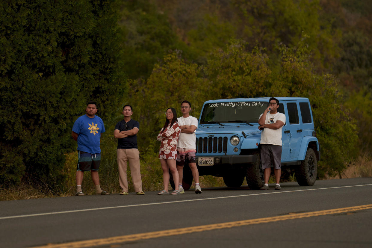 People watch a hillside burn from a highway.