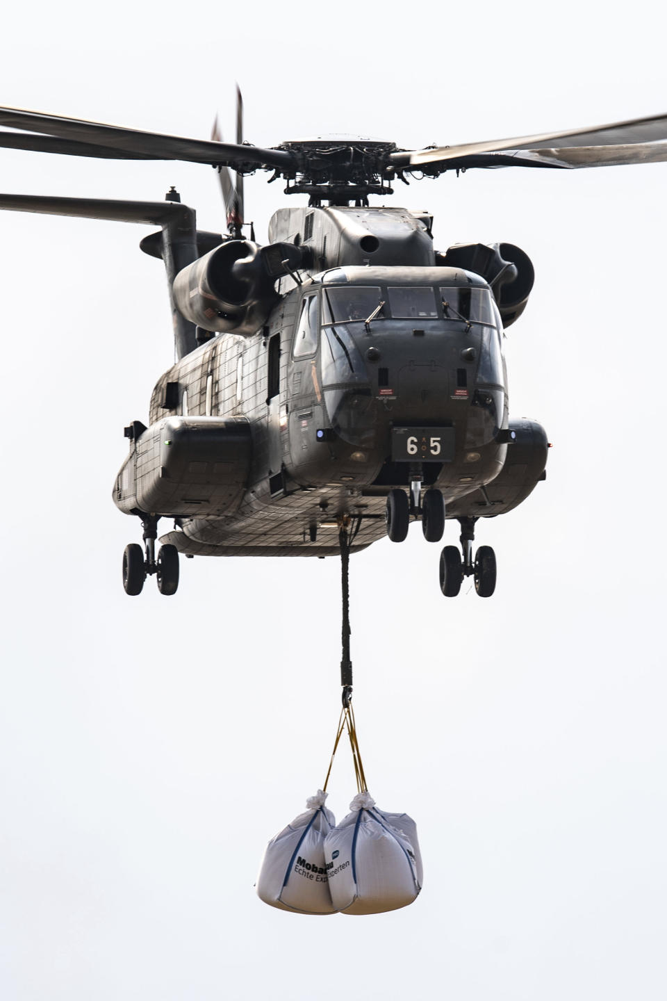 A Bundeswehr CH-53 transport helicopter picks up big bags of ballast in Ergfstadt, Germany, Thursday July 22, 2021, to fly them to the Blessem district to damn up the banks of the Erft river. In the flood disaster area of Erftstadt-Blessem, some residents are being allowed back into their homes to clear debris after heavy rains caused devastating floods. (Marius Becker/dpa via AP)