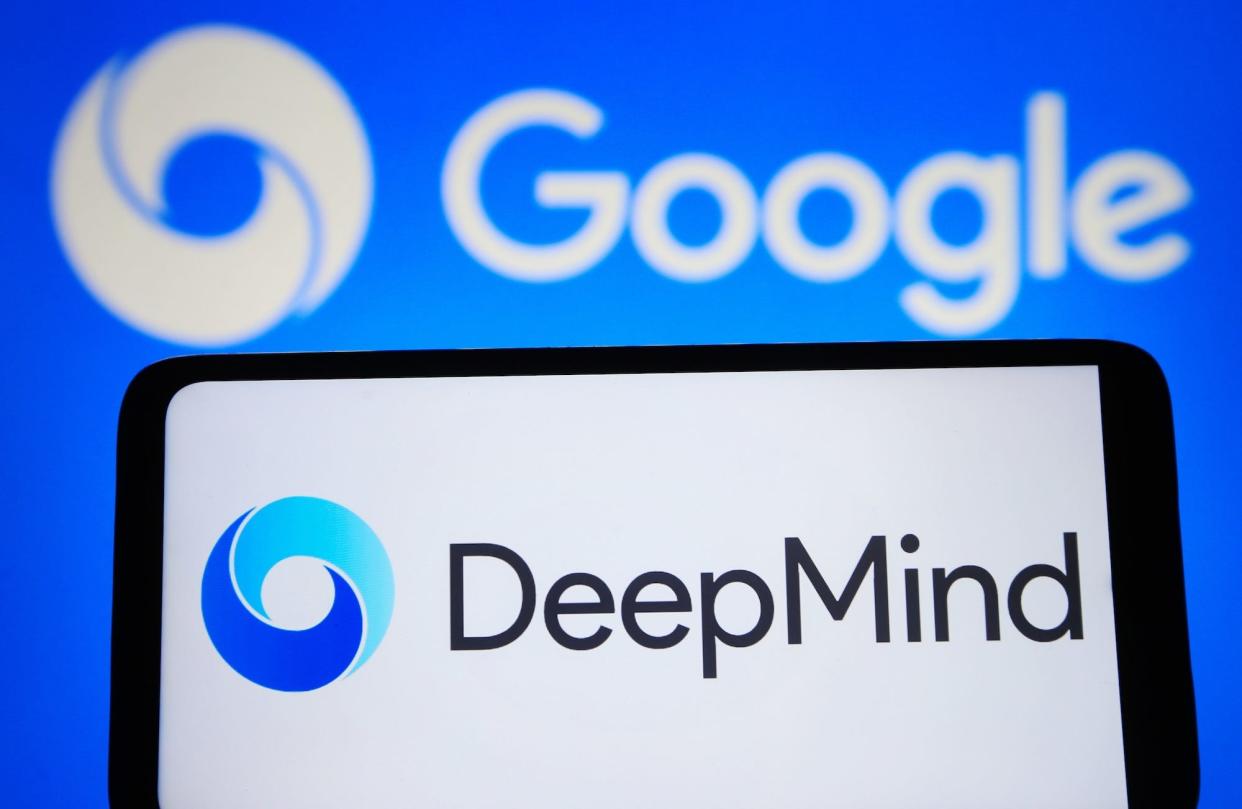 A smartphone displays the DeepMind logo in front of a blurred Google logo in the background.