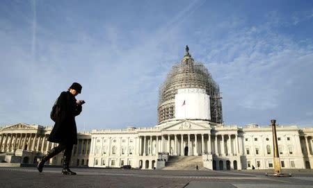 A woman checks her smartphone as she walks past the U.S. Capitol in Washington December 4, 2014. REUTERS/Kevin Lamarque