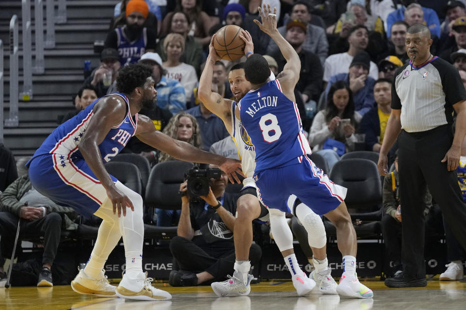 Golden State Warriors guard Stephen Curry, right rear, looks to pass the ball while being defended by Philadelphia 76ers center Joel Embiid, left, and guard De'Anthony Melton (8) during the first half of an NBA basketball game in San Francisco, Friday, March 24, 2023. (AP Photo/Jeff Chiu)