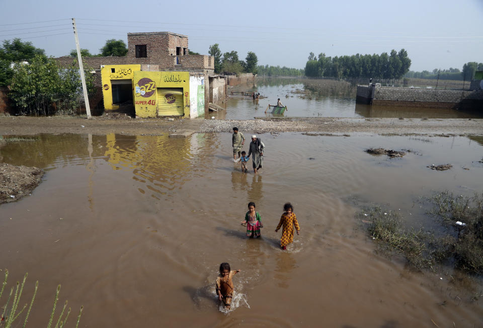 People wade through floodwaters, in Charsadda, Pakistan, Wednesday, Aug. 31, 2022. Officials in Pakistan raised concerns Wednesday over the spread of waterborne diseases among thousands of flood victims as flood waters from powerful monsoon rains began to recede in many parts of the country. (AP Photo/Mohammad Sajjad)