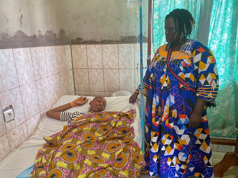 Edwin Ojong Ayuk Mbeng stands beside her son Blessing Mbeng, 13, who was shot by gunmen after they stormed his school, as he lies in a hospital bed in Kumba