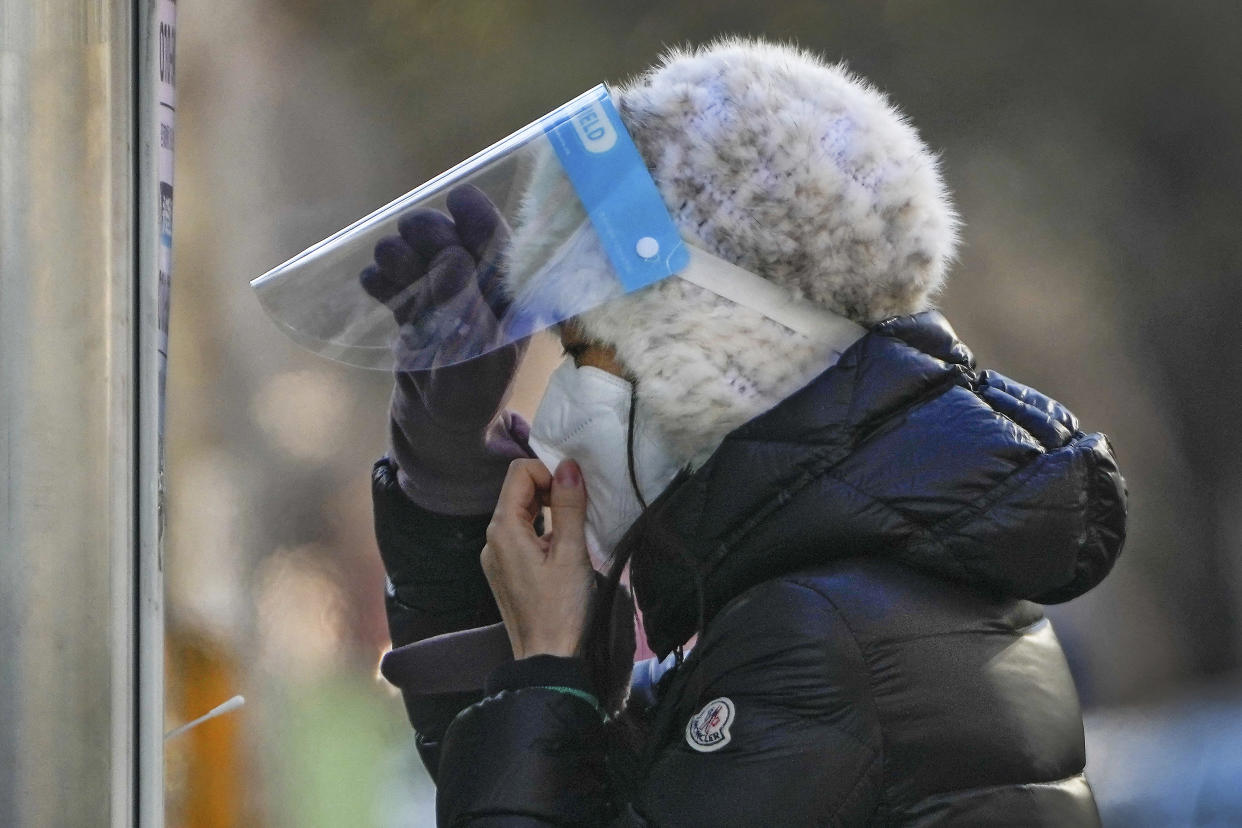 A woman wearing a face mask and face shield get ready for her routine COVID-19 throat swab at a coronavirus testing site in Beijing, Wednesday, Dec. 7, 2022. China has announced new measures rolling back COVID-19 restrictions, including limiting lockdowns and testing requirements. (AP Photo/Andy Wong)