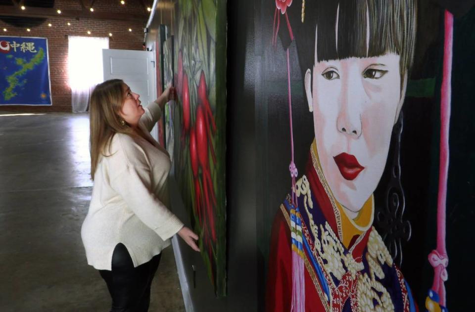 Karen Ouzts, founder and owner of the Heritage Art Center in Columbus, Georgia, adjusts one of the paintings being shown in “Wanderlust & Art.” The show features nearly 300 works by Dorota Quiroz, an artist with more than 30 years of professional experience who specializes in large scale works in oils, including murals and portraits.