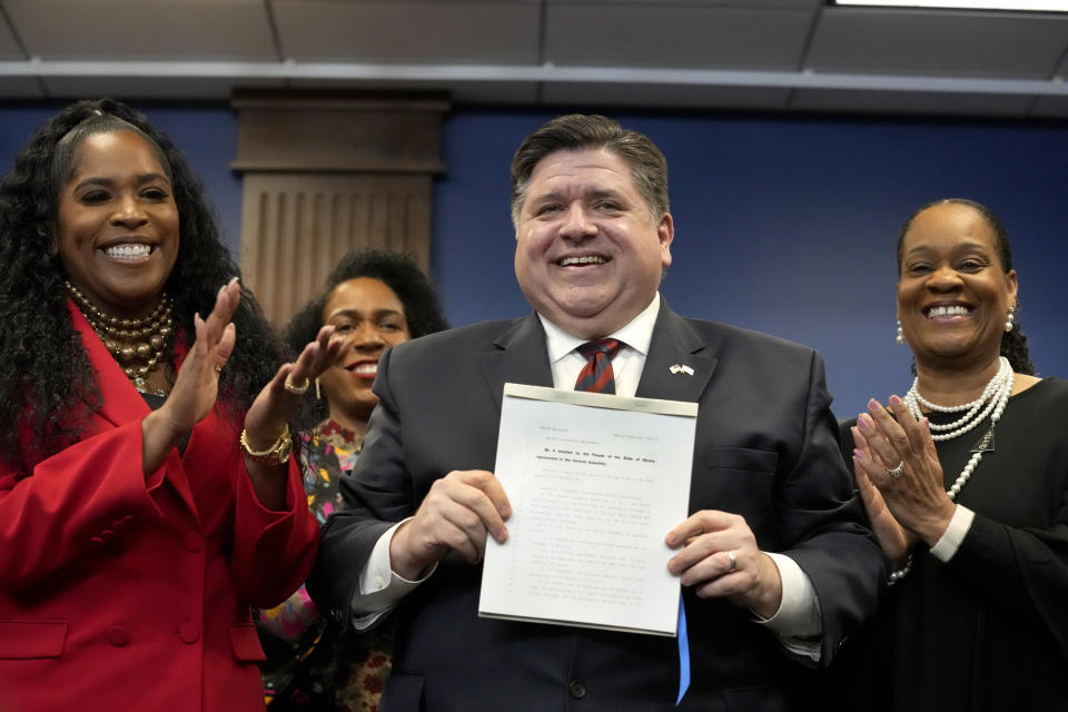 Illinois Gov. J.B. Pritzker displays the newly signed Paid Leave For All Workers Act as Illinois House Speaker pro-tem Jehan Gordon Booth, left, Lt. Gov. Juliana Stratton, second from left, and Senate Majority Leader Kimberly Lightford applaud on Monday, March 13, 2023, in Chicago. Illinois became one of three U.S. states to require employers to offer paid time off for any reason starting in January of 2024. (AP Photo/Charles Rex Arbogast)
