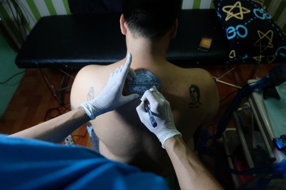 A tattoo artist outlines a design with Burmese text that reads "spring revolution" on the back of a man with other tattoos that depict the anti-coup three-fingered protest salute and deposed Myanmar leader Aung San Suu Kyi in Yangon, Myanmar Thursday, Mar. 25, 2021. (AP Photo)