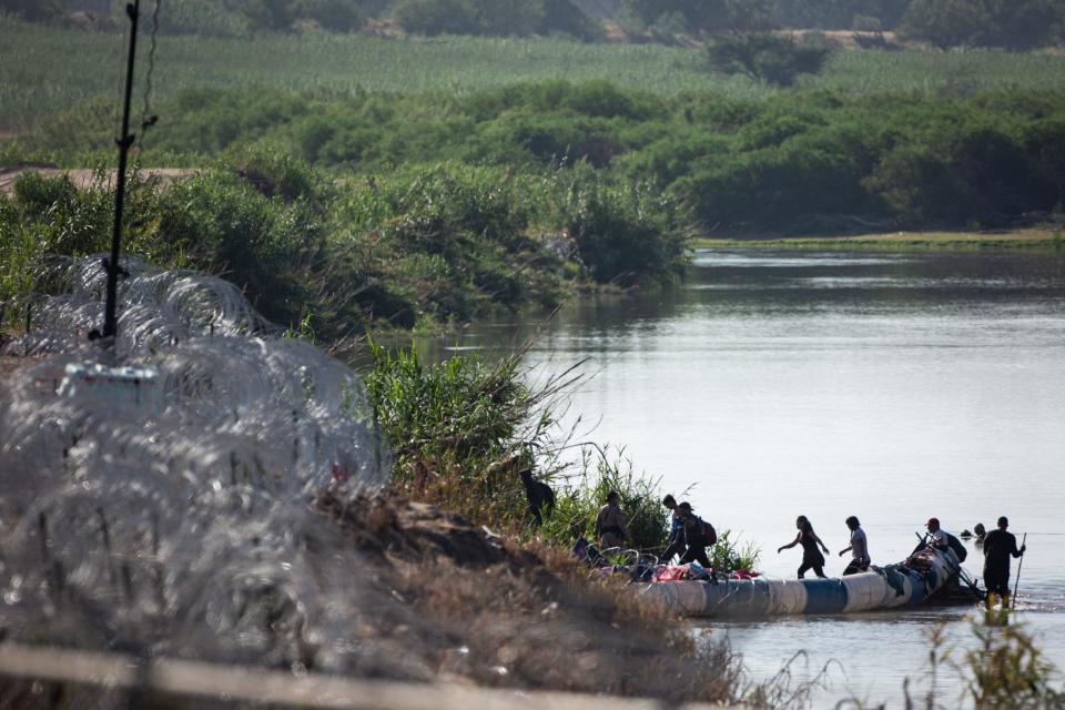 Migrants are directed by a DPS Trooper around floating barrels covered in razor wire in the Rio Grande on Saturday, July 22, 2023, in Eagle Pass, Texas. Migrants travel miles along the riverbank to the edges of the wire placed under Operation Loan Star.