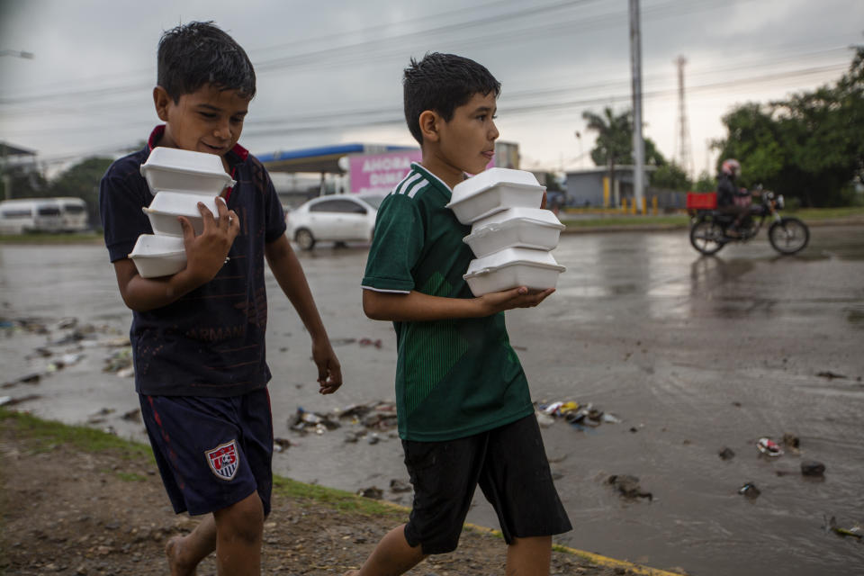 Youths carry donated hot meals back to their tents alongside a highway where they live with others after last year's hurricanes Eta and Iota left their family's homeless in San Pedro Sula, Honduras, Tuesday, Jan. 12, 2021. The World Food Program says the number of Hondurans facing food insecurity is 3 million, six times higher than before. (AP Photo/Moises Castillo)