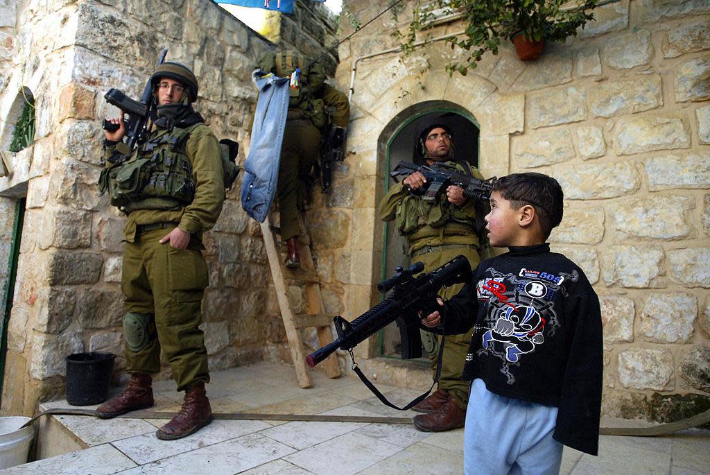 A Palestinian boy plays with his plastic rifle as Israeli soldiers search homes and rooftops in the West Bank town of Hebron in this file photo from 29 December 2006: AFP/Getty Images