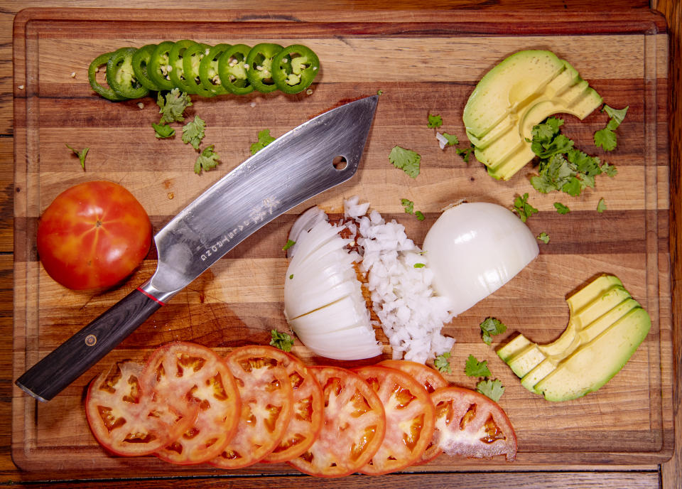 Dalstrong's 8" Phantom Series Chef and Cleaver Hybrid Knife rests on a wooden cutting board alongside sliced tomatoes, a diced white onion, sliced avocado, and sliced jalapeños.