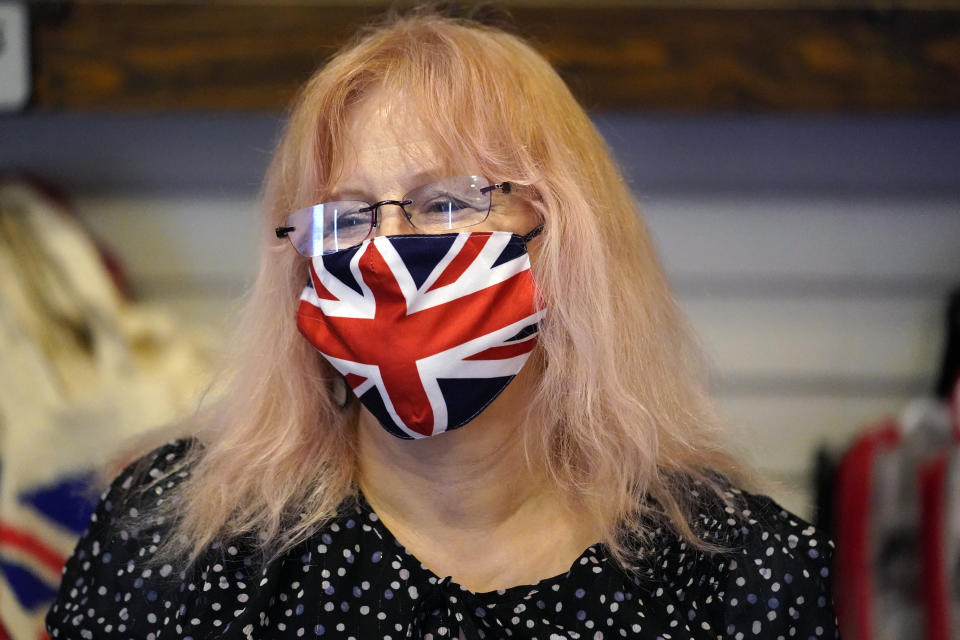 Helen Dawson wears a mask of the British flag while tending to customers at Ye Olde King's Head Shoppe on Thursday, Nov. 19, 2020, in Santa Monica, Calif. The British restaurant and bar in seaside Southern California has been battered the past nine months and was in the process of adapting to new restrictions that took effect Friday, Nov. 20 that would further crimp its recovery even as the prospect of a crippling shutdown loomed. (AP Photo/Marcio Jose Sanchez)