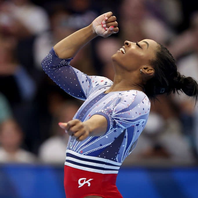 Simone Biles celebrates after completing a gymnastics routine at a competition. She is wearing a leotard with sparkly details