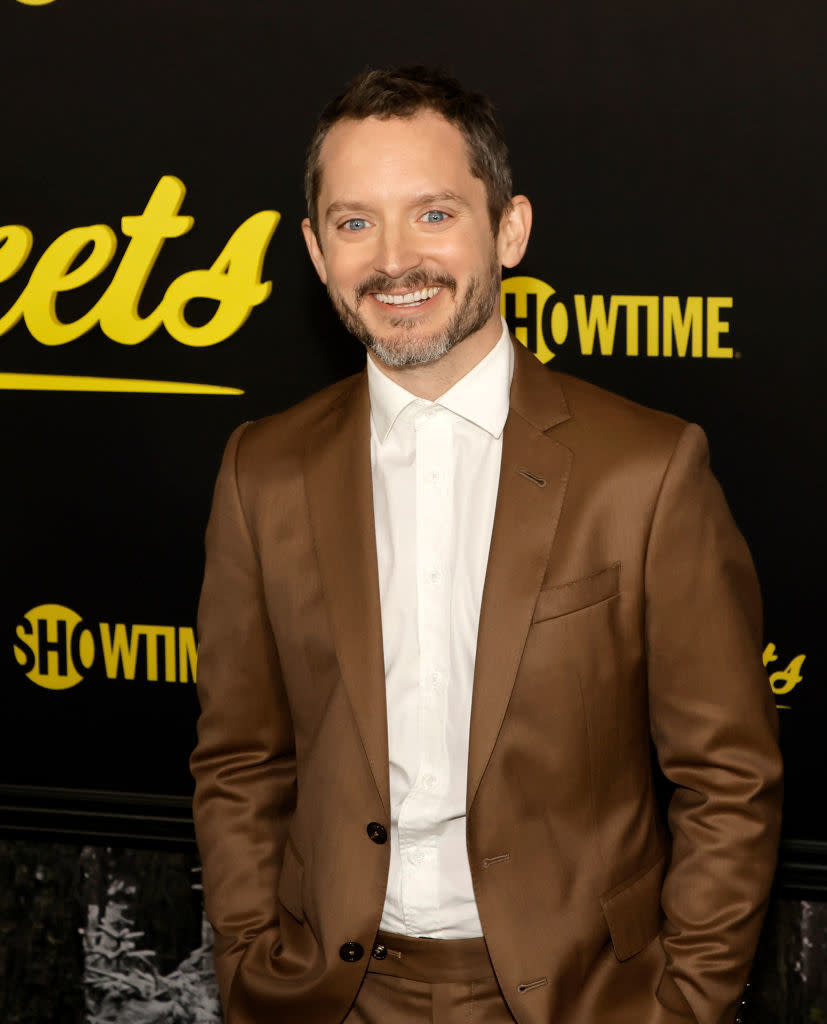 Close-up of Elijah smiling in a suit at a media event