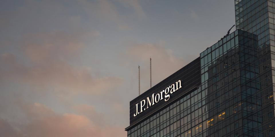 A glass office building at dusk, with JPMorgan logo in white on a black background on its top corner.
