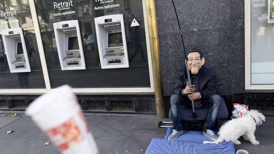 Un hombre pidiendo dinero enfrente de un cajero.