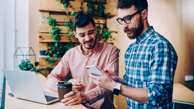 Disappointed male it developers stressed with application problem using technology for distance job, young hipster guys annoyed with bad news making booking via telephone and discussing solution - Image.