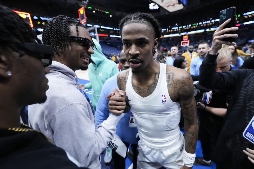 Memphis Grizzlies guard Ja Morant (12) greets LSU quarterback and NCAA football Heisman Trophy winner Jayden Daniels, left, after scoring the game-winning basket at the buzzer in the second half of an NBA basketball game against the New Orleans Pelicans in New Orleans, Tuesday, Dec. 19, 2023. The Grizzlies won 115-113. (AP Photo/Gerald Herbert)