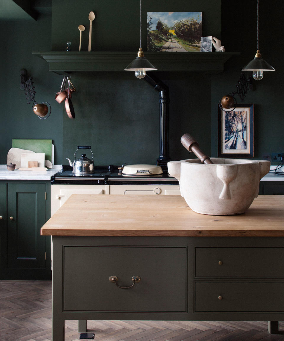 A kitchen island in a dark green painted farmhouse kitchen with cream Aga.