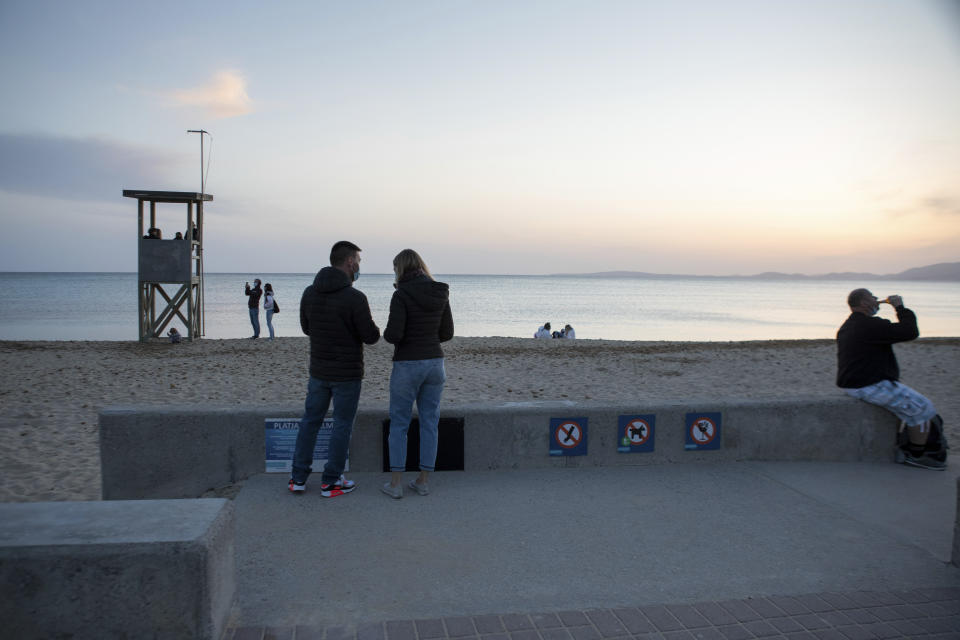 Tourists stand on a beach during sunset at the Spanish Balearic Island of Mallorca, Spain, Saturday, March 27, 2021. Efforts in Spain to restart tourism activity is drawing a mixed picture due to a patchwork of national, regional and European rules on travel that is confusing both tourists and their hosts. (AP Photo/Francisco Ubilla)