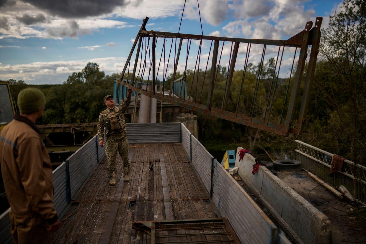 Ukrainian soldiers remove metal structure pieces as they work on a bridge damaged during fighting with Russian troops in Izium, Ukraine, Monday, Oct. 3, 2022. 